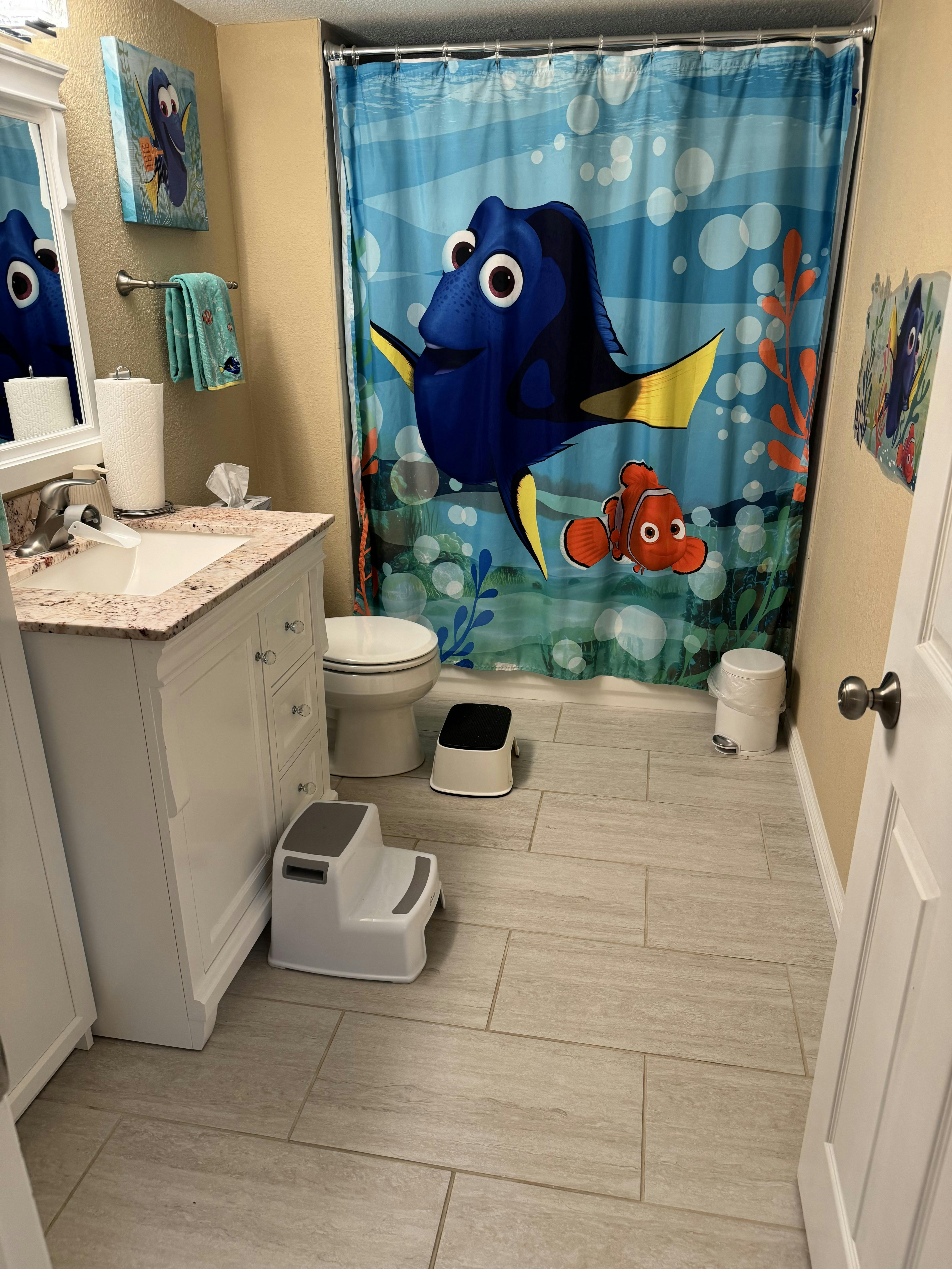 Finding Dory themed bathroom with shower curtain, vanity, toilet, and step stools