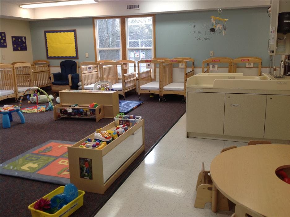 Empty infant nursery room with cribs, play mats, changing station, and toys