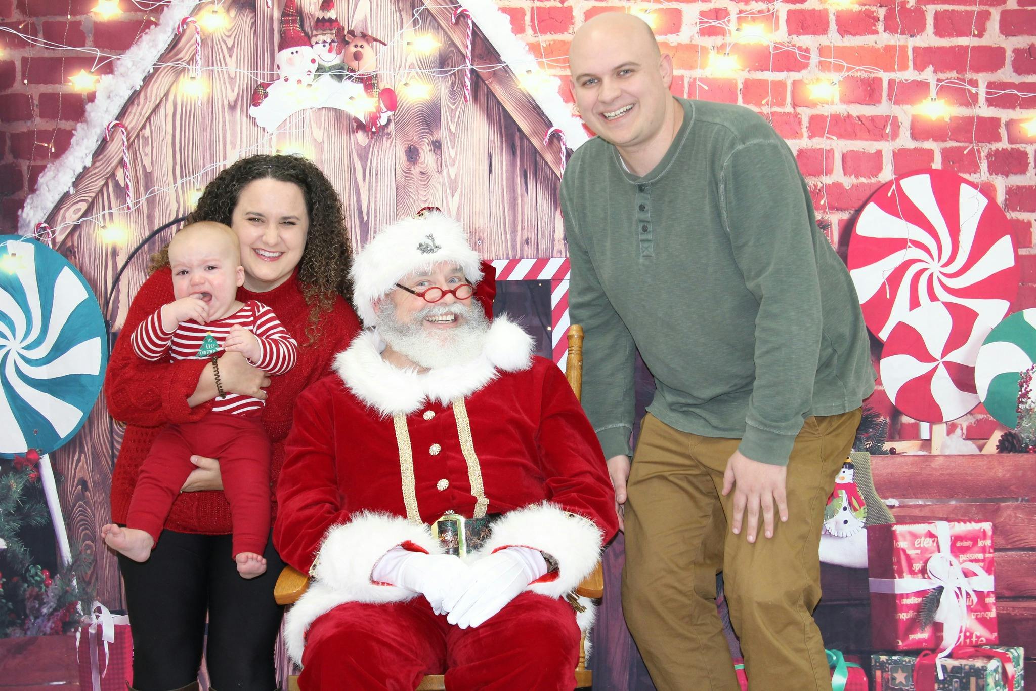 Person holding a child, person in Santa costume, and another person standing