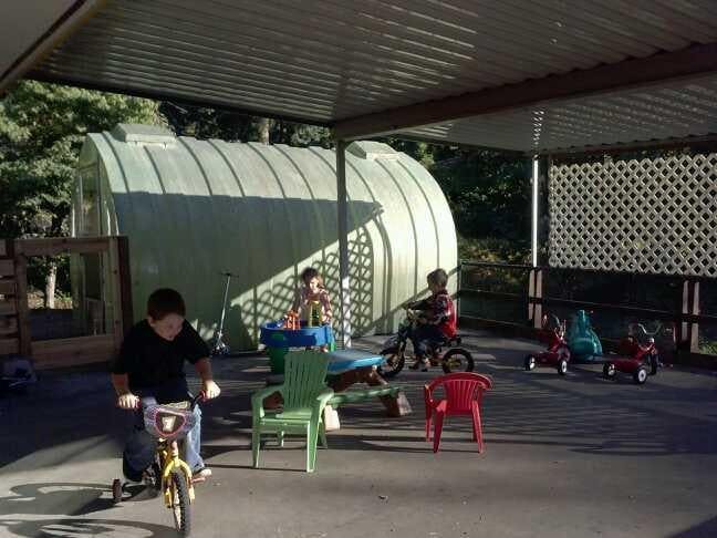 Child riding a bicycle under a covered patio with other children and toys