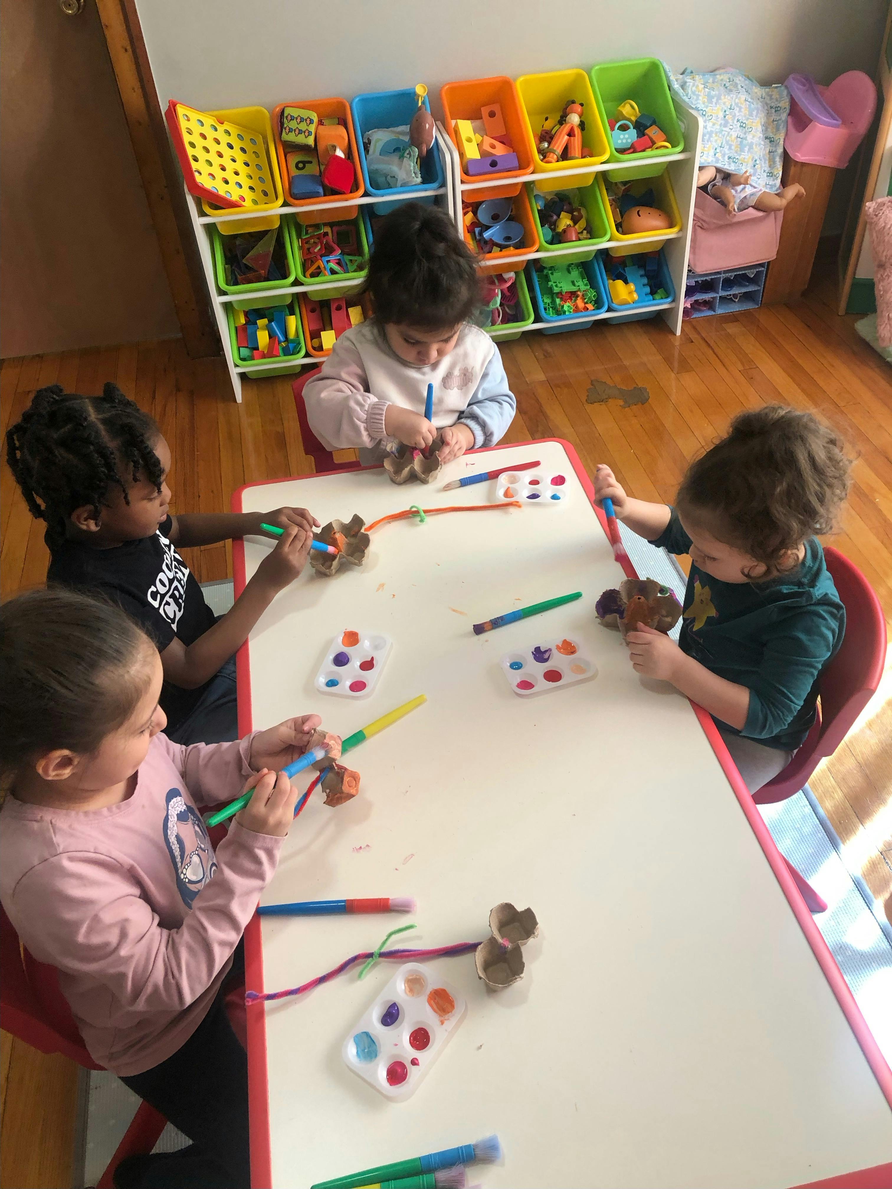 Four children painting with brushes at a table