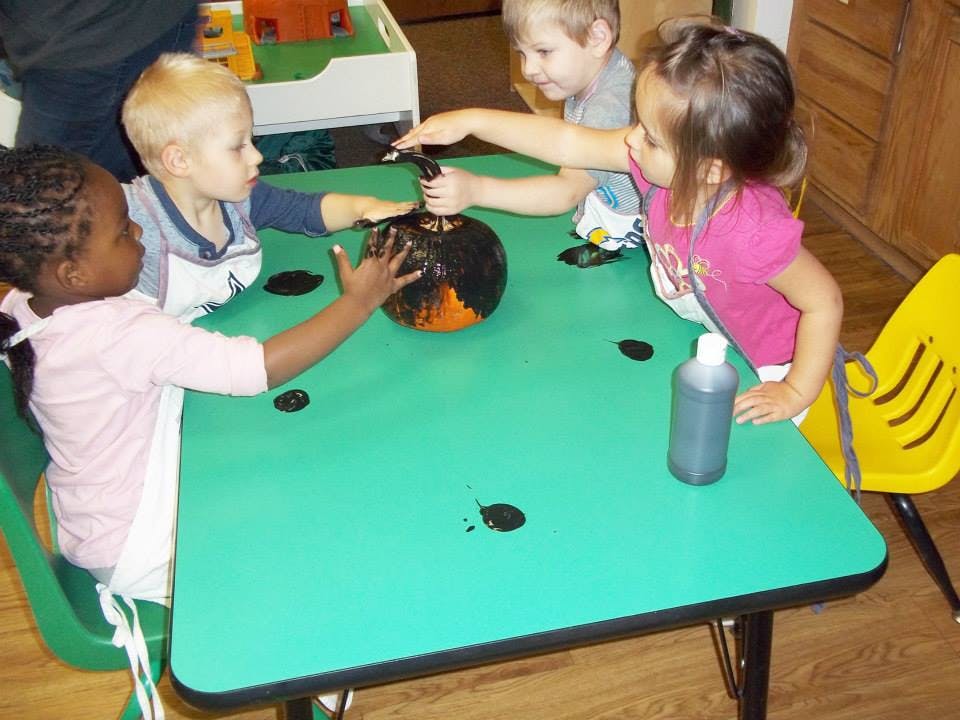 Children painting a pumpkin at a table