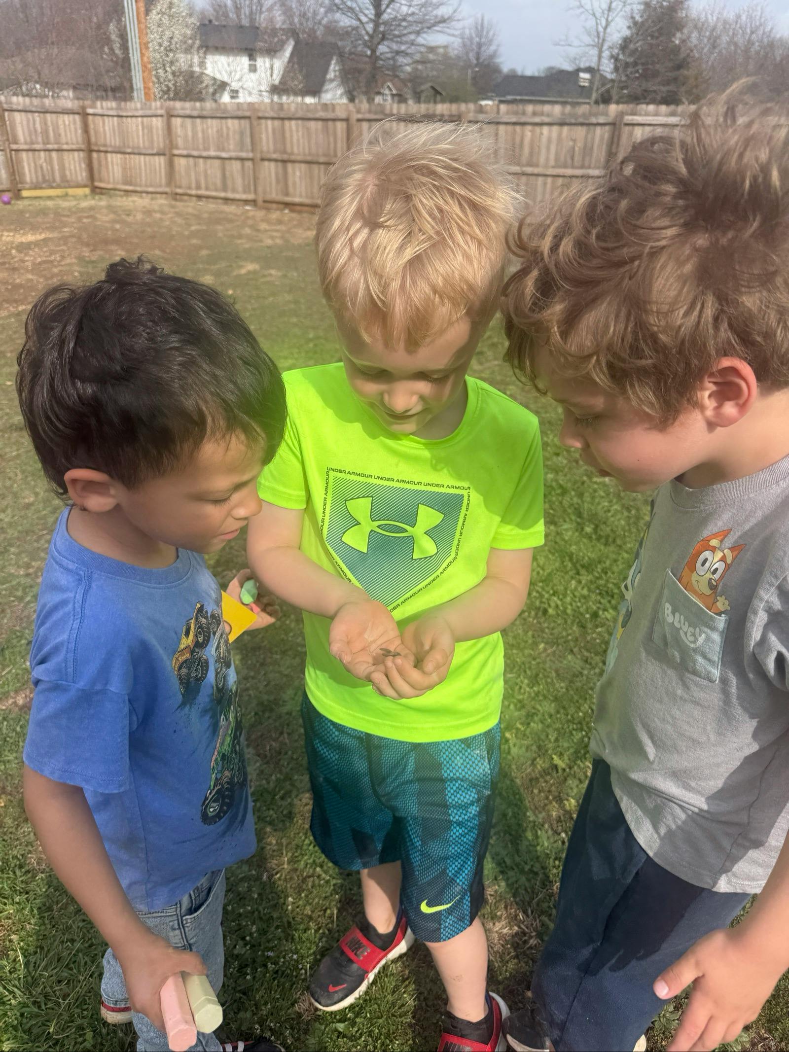 Three children looking at something in a child's hands outdoors