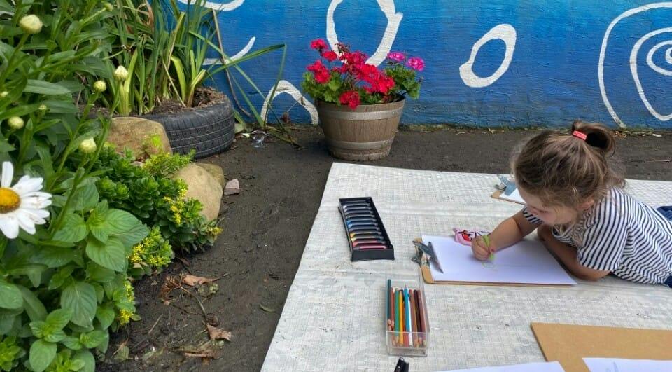 Child drawing with colored pencils on a paper mat outdoors