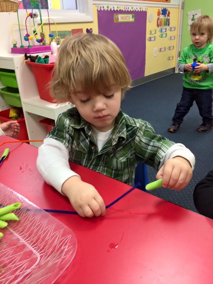 Child at red table working with pipe cleaners and pasta