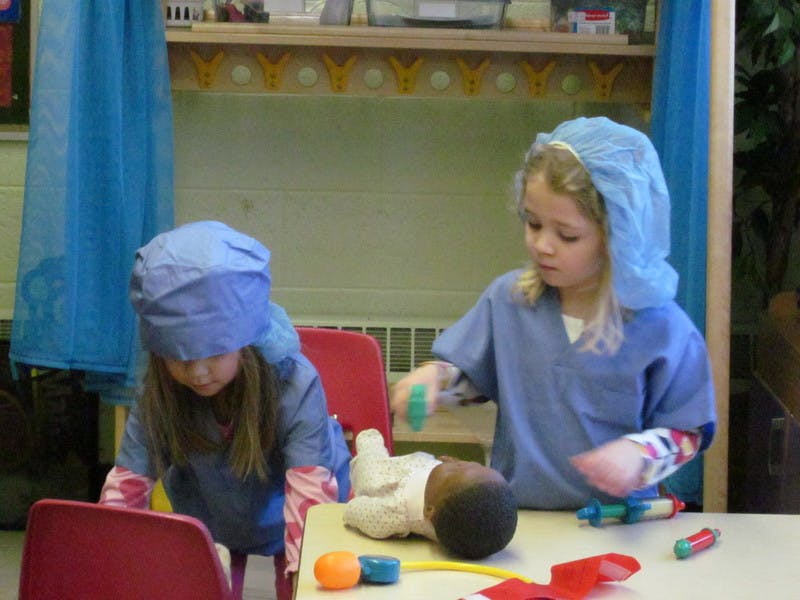 Two children in scrubs playing with a doll