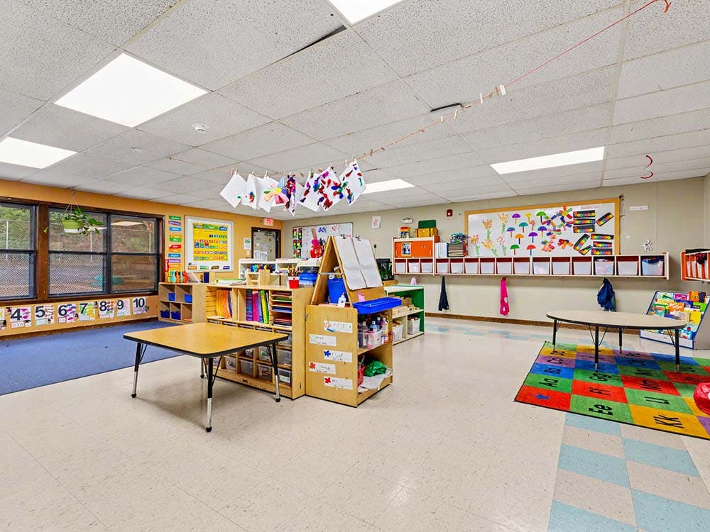 Classroom with tables, shelves, whiteboards, and children's artwork displayed