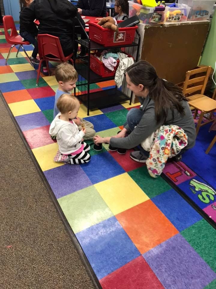 Adult and two children playing on a colorful floor