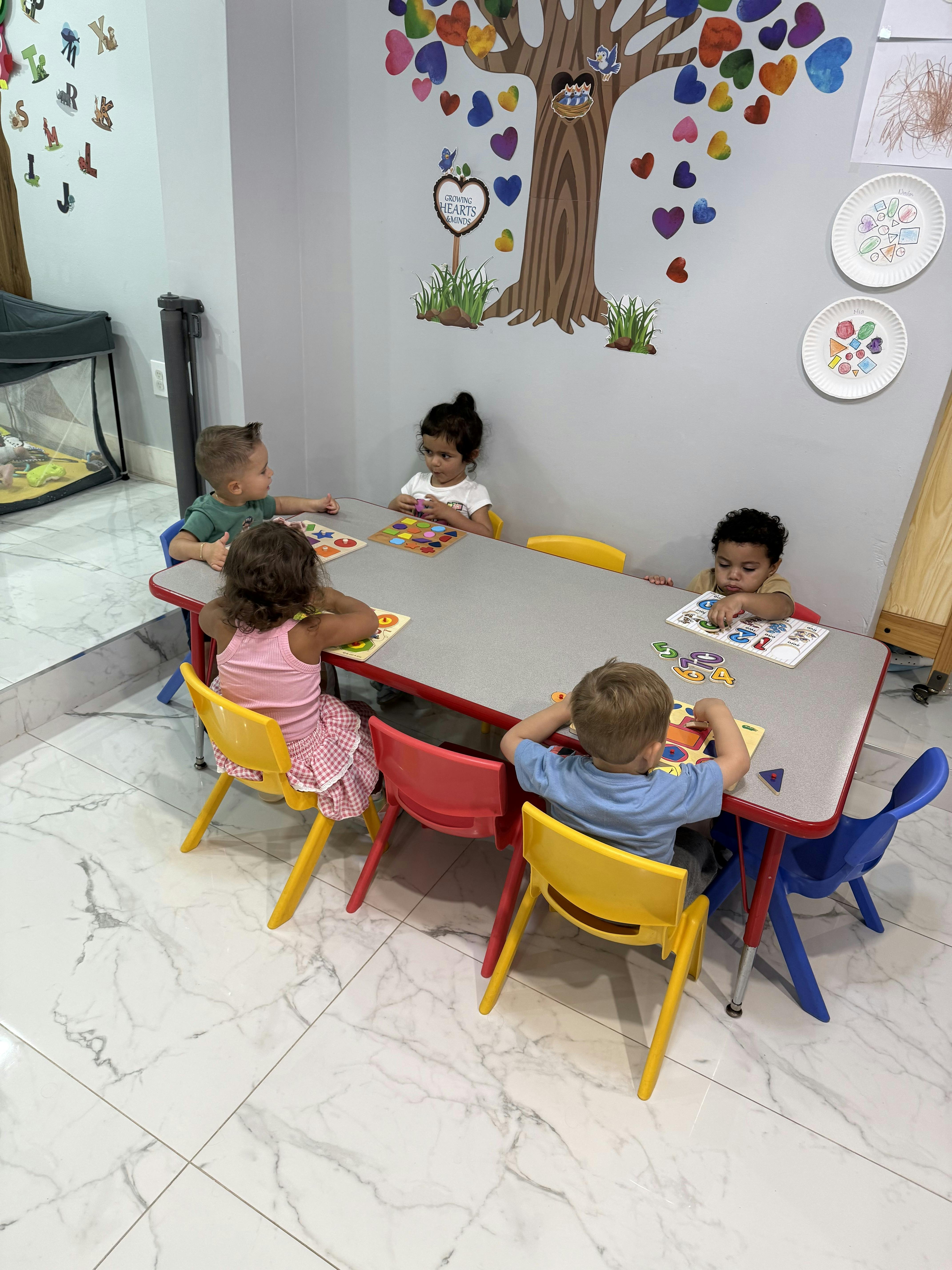 Five children sitting at a table playing with educational puzzles in a classroom