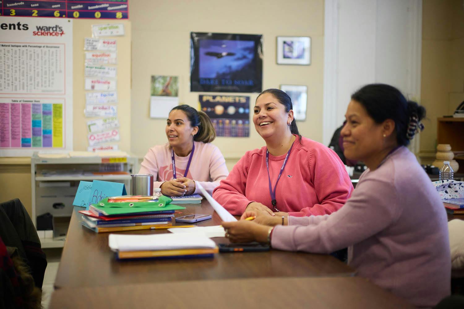 Three people sitting at a table in a classroom