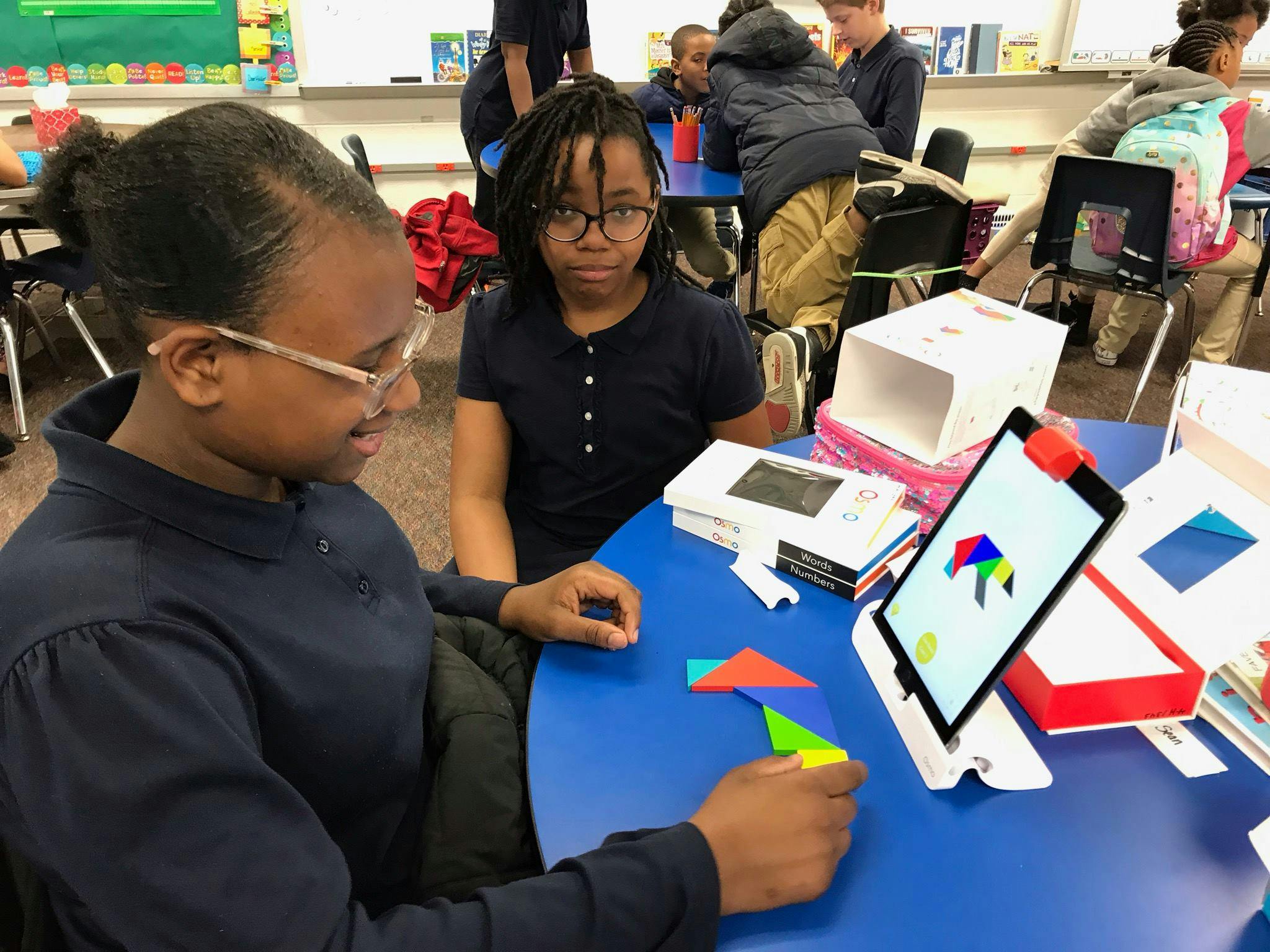 Two teens at a table with a tablet and colorful geometric shapes