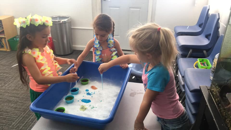 Three children playing with water in a blue bin