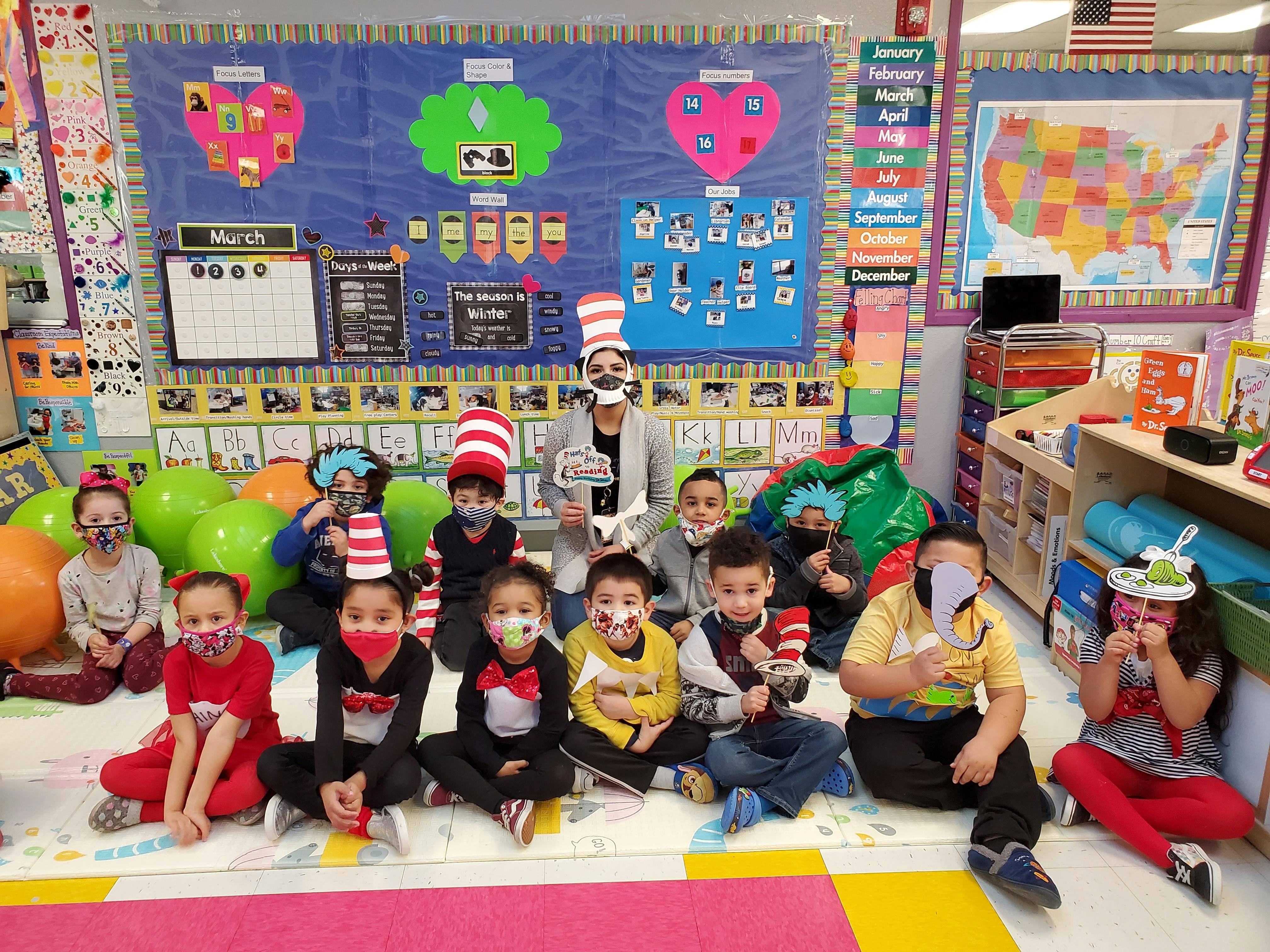 Adult and children in a classroom wearing masks and Dr. Seuss-themed hats