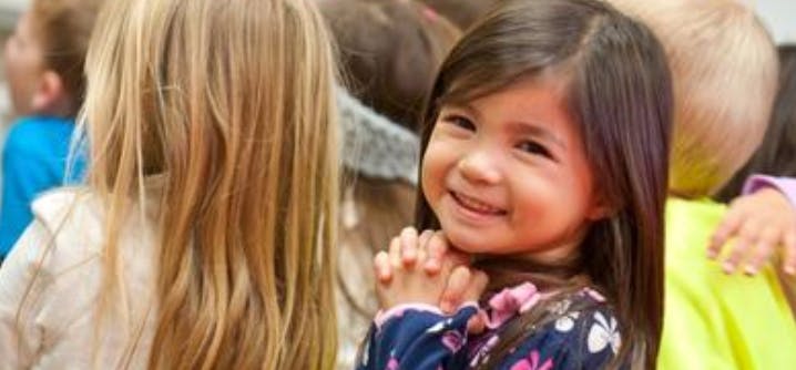 Child smiling with hands clasped in front of other children