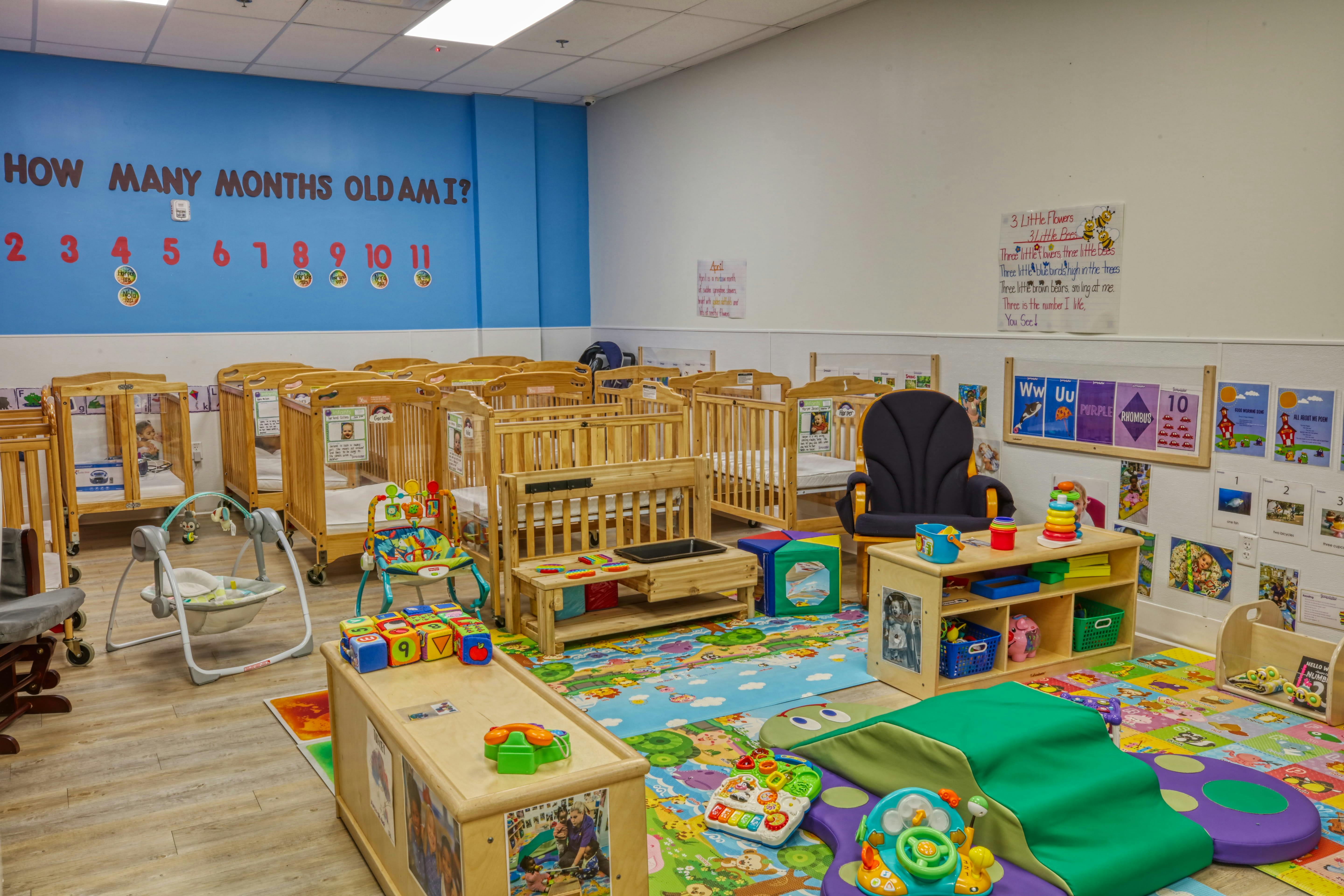 A colorful childcare room with many cribs, play mats, and toys