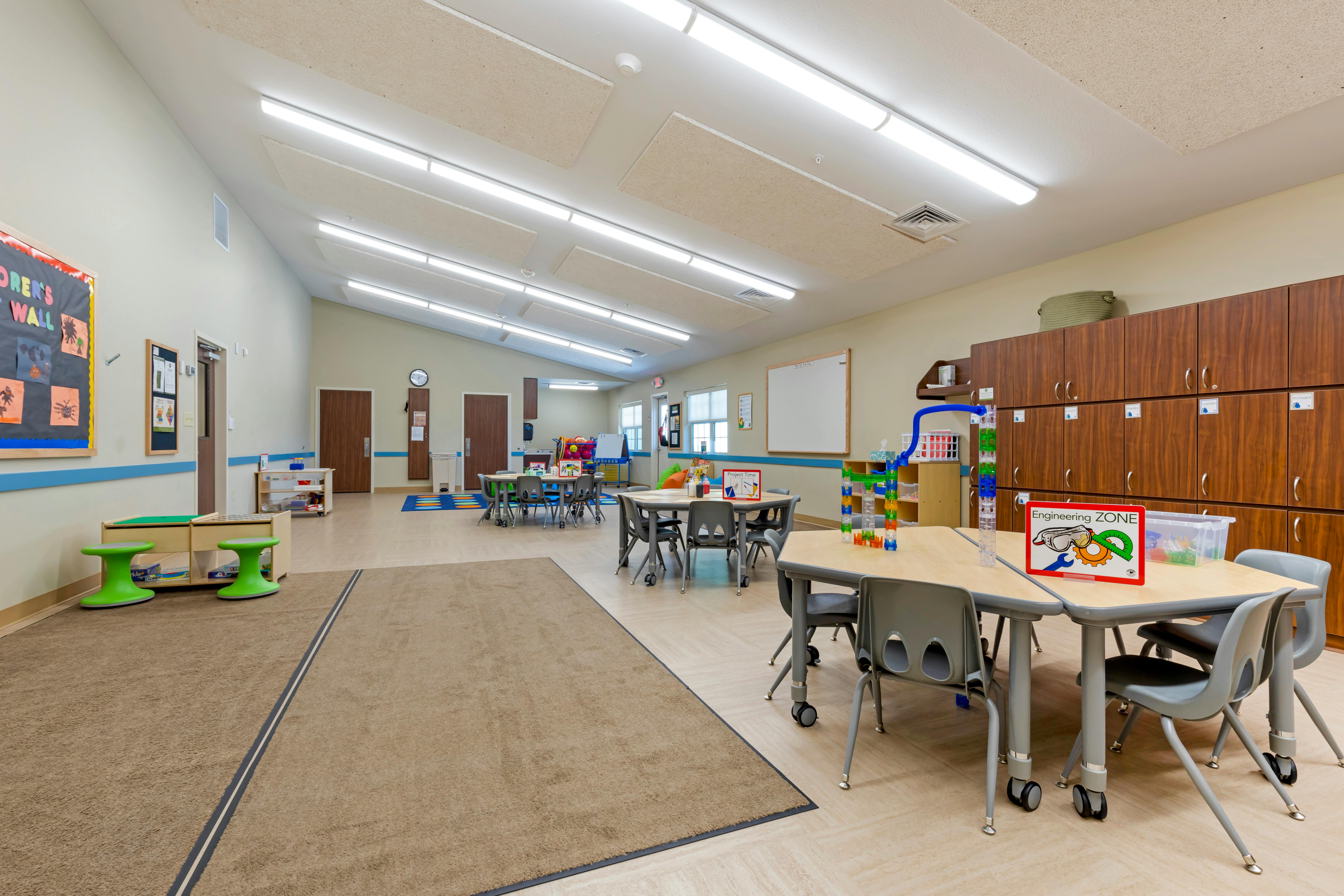 Classroom with child-sized tables and chairs, a brown rug, and cabinets