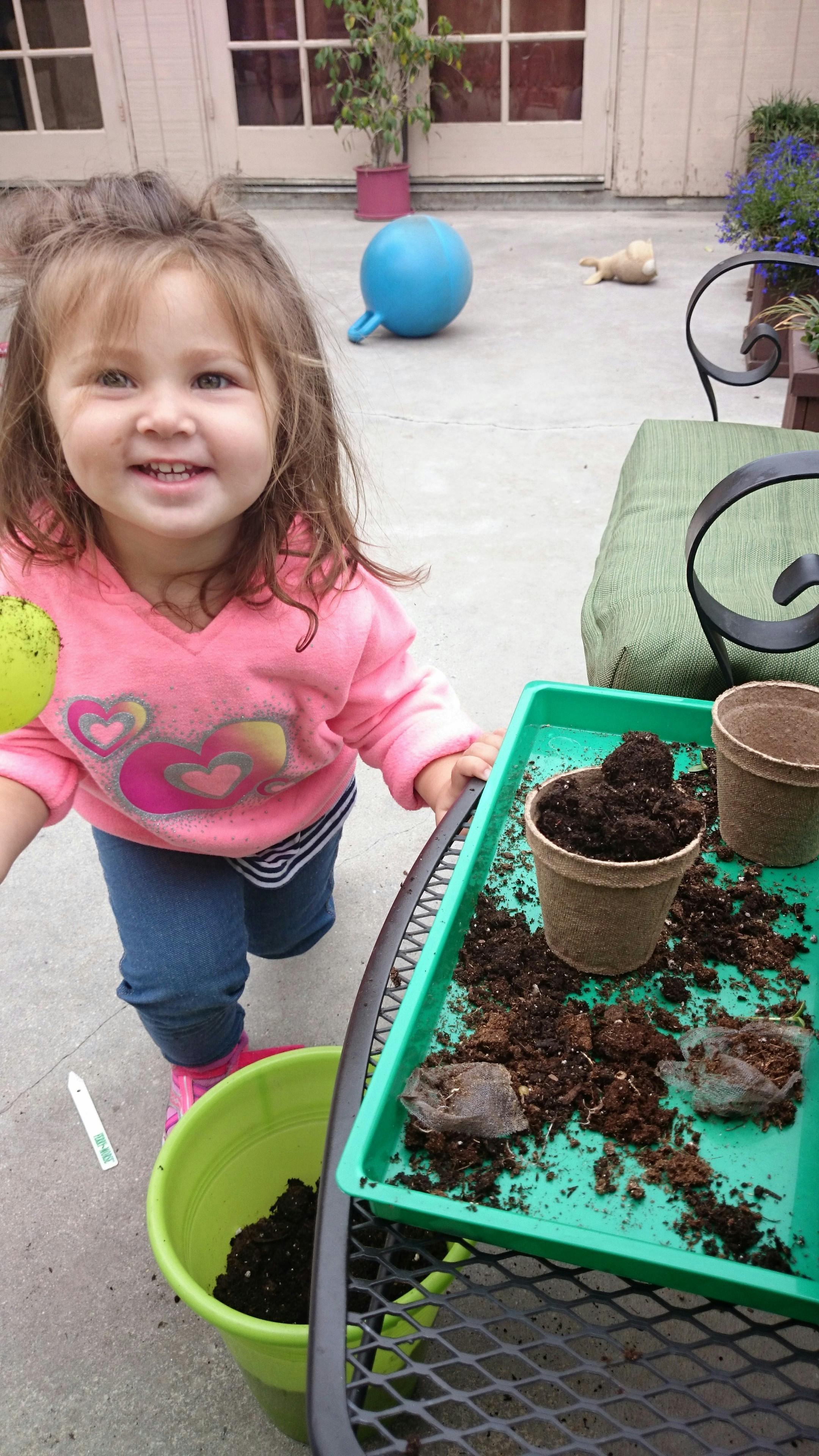 Child standing next to a tray with soil and pots