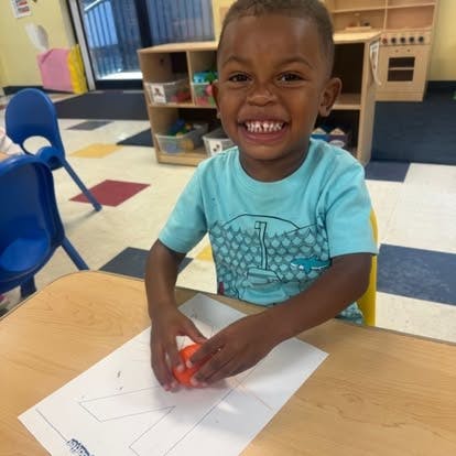 Child sitting at a table with a paper and playing with a small orange object
