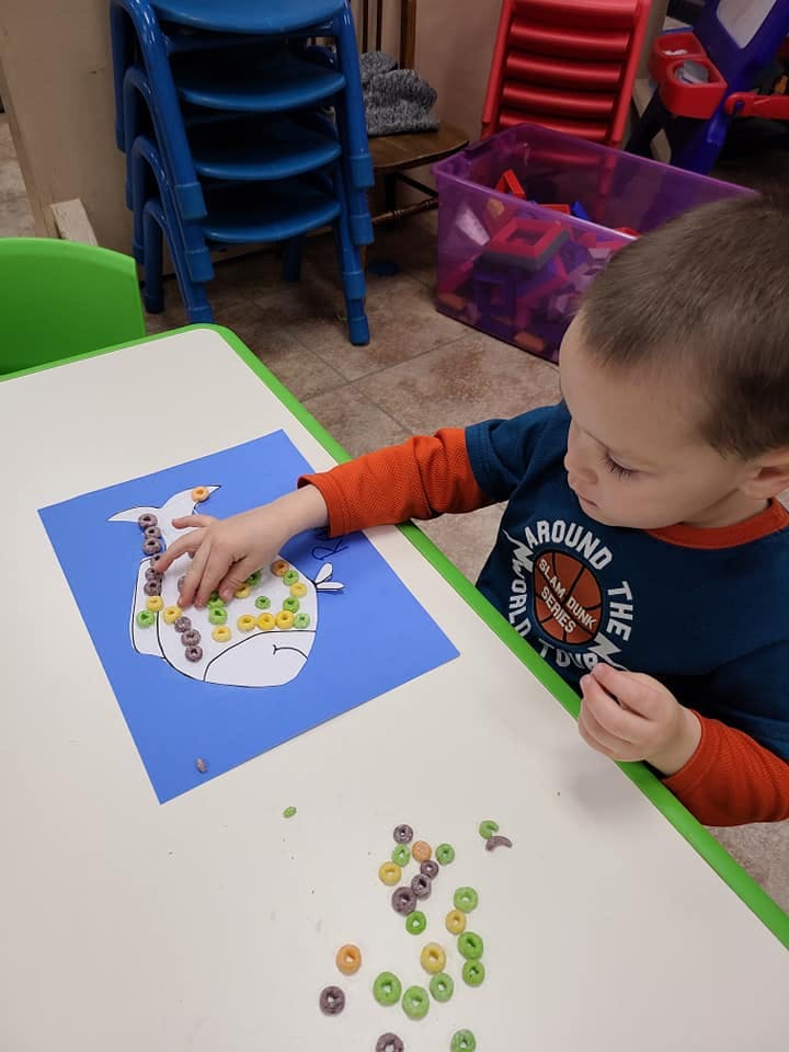 Child doing an art activity with cereal on a whale cutout