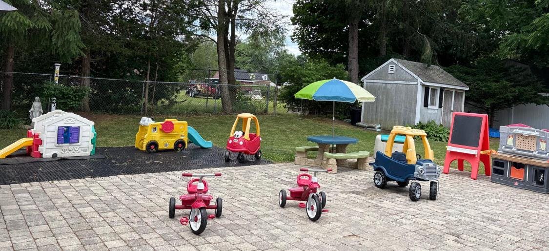 Plastic ride-on toys, tricycles, and play equipment on a backyard patio