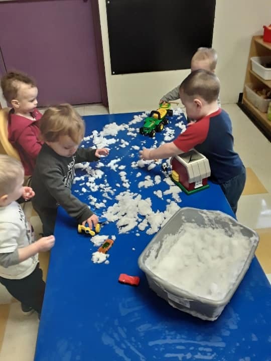 Children playing with toys and white fluffy material on a blue table