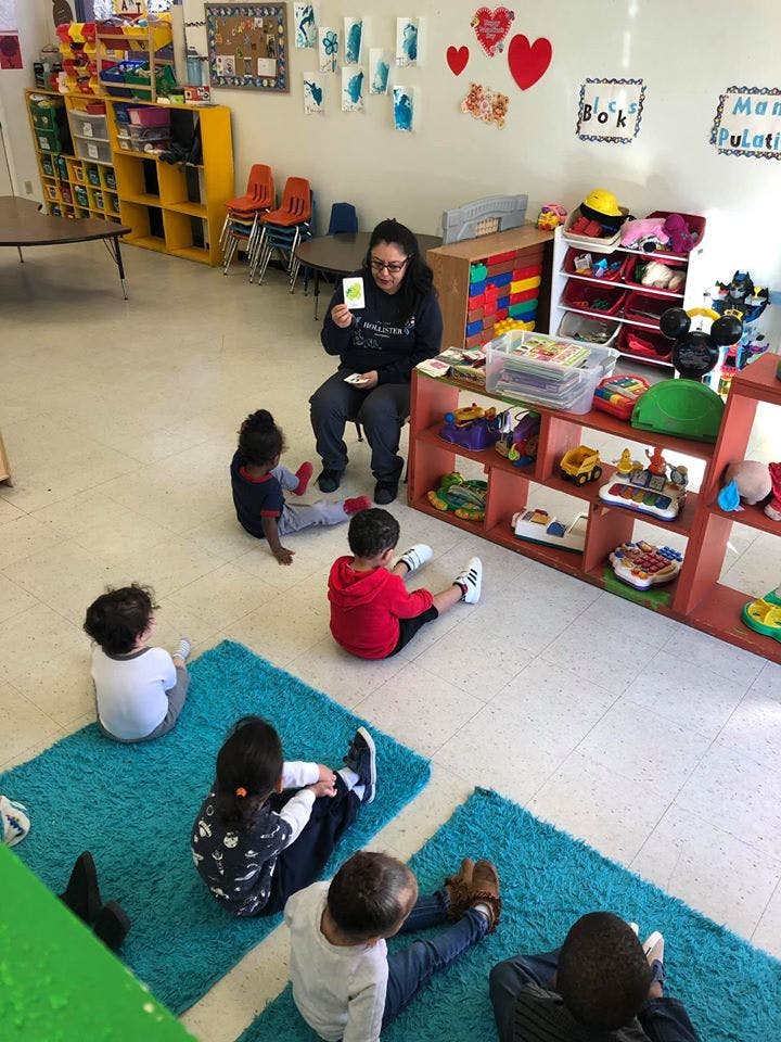 Person holding up a card to a group of children sitting on the floor in a classroom