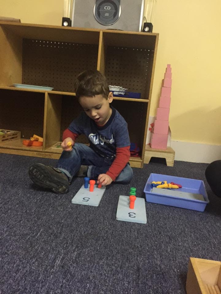 Child playing with colorful pegs on numbered boards in a classroom