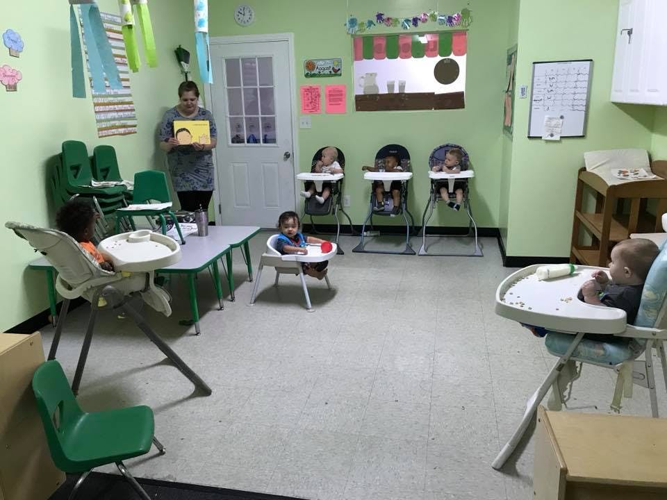 Person holding a book in a room with multiple children in high chairs
