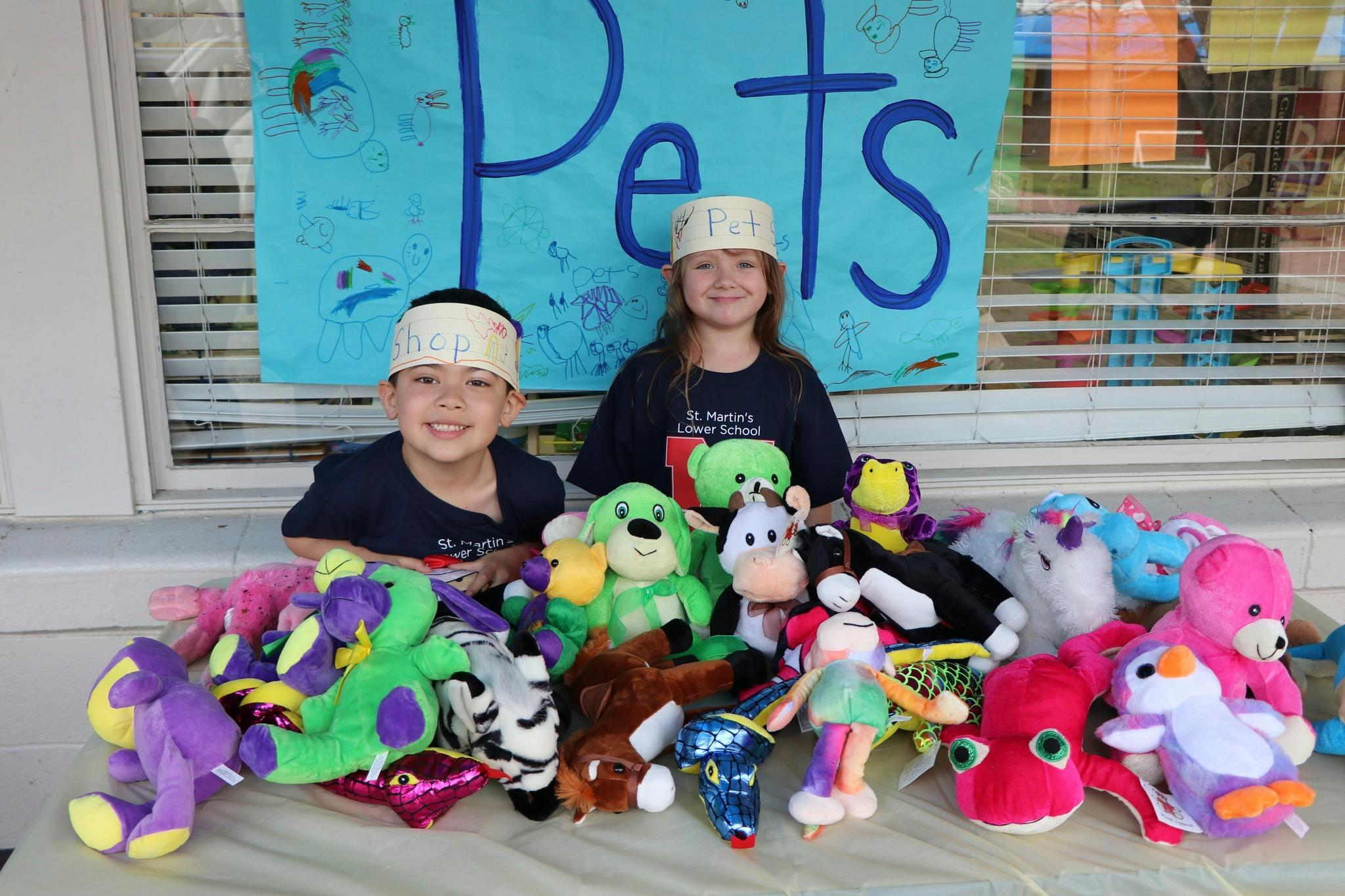 Two children with headbands sitting behind a table full of stuffed animals