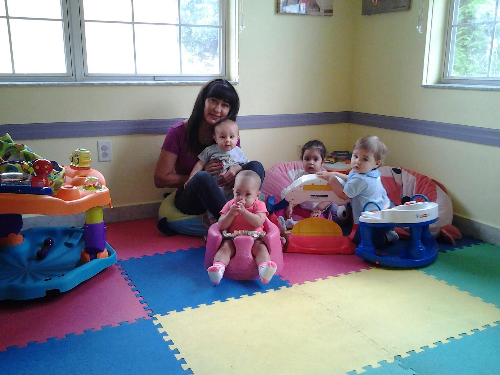 Person holding a child, with three other children in baby seats on a colorful mat