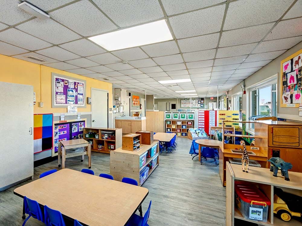 Empty classroom with small tables and chairs, shelves, and learning materials