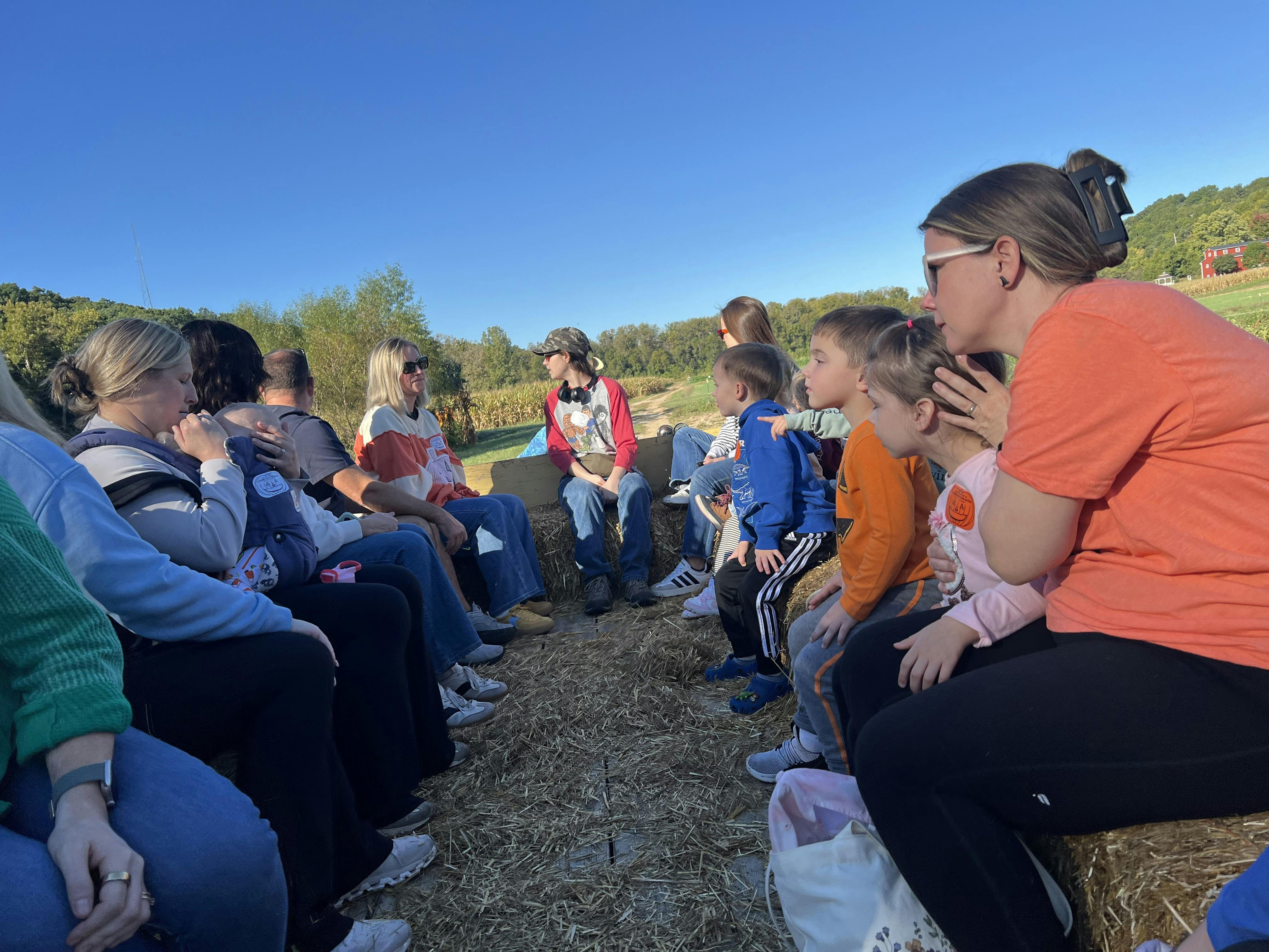 Group of people sitting on straw bales on a wagon outdoors