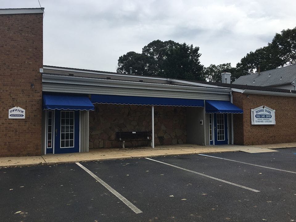 Building exterior with blue awnings over doors and a parking lot in front