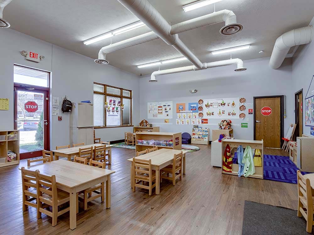 Classroom with small wooden tables and chairs, and an exit door