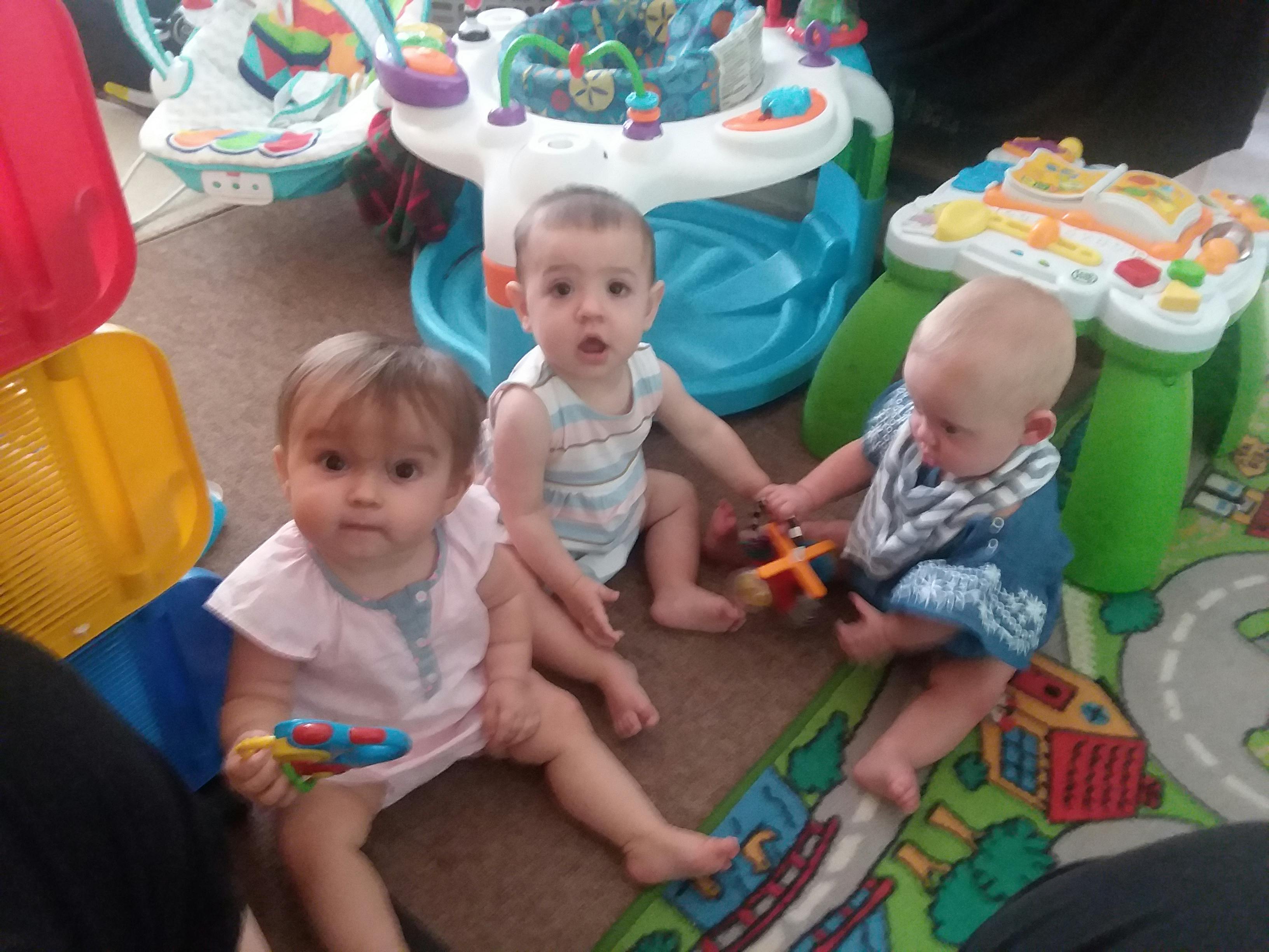 Three children sitting on a rug with toys
