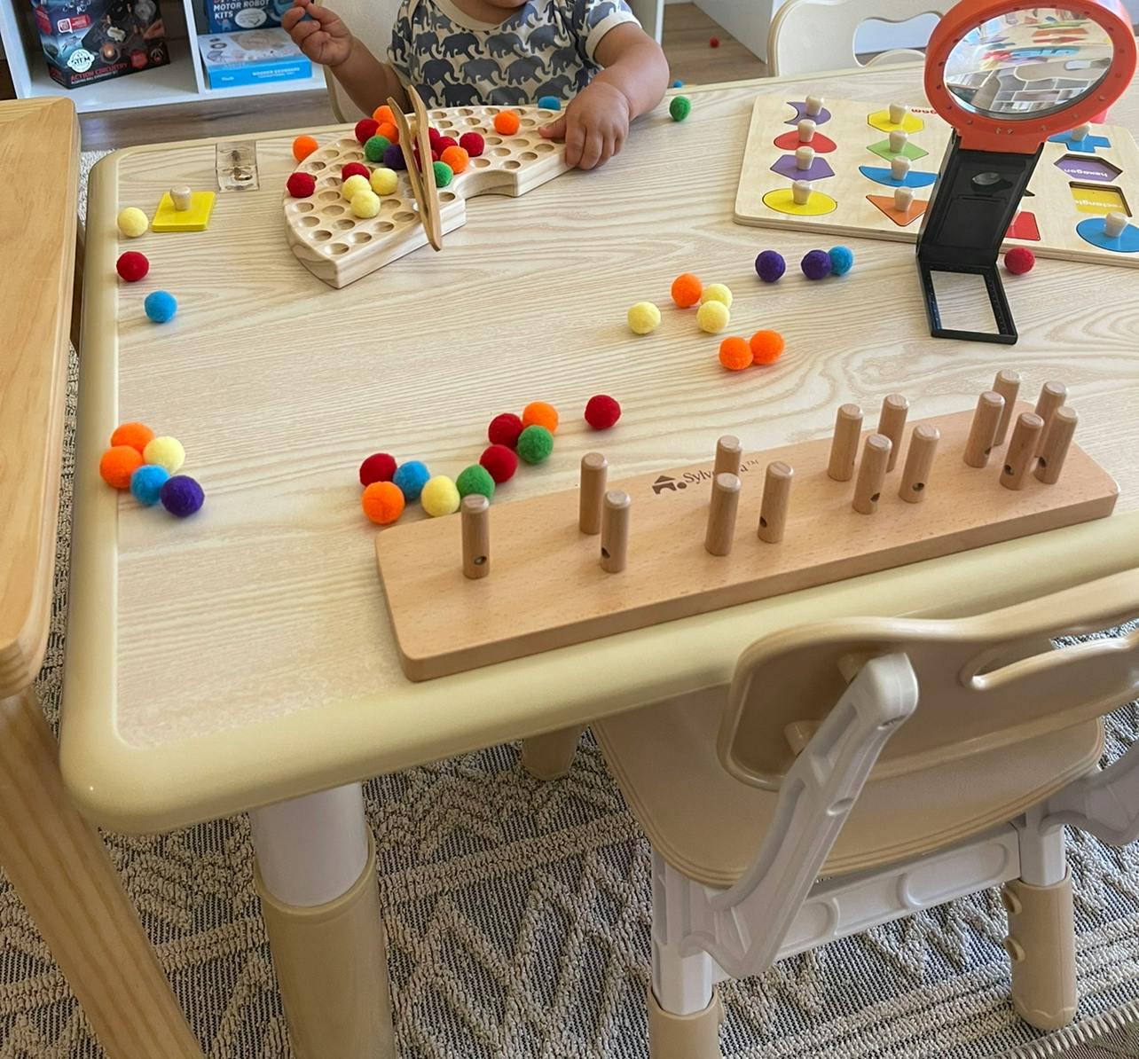 Child playing with colorful pom-poms and wooden toys on a table