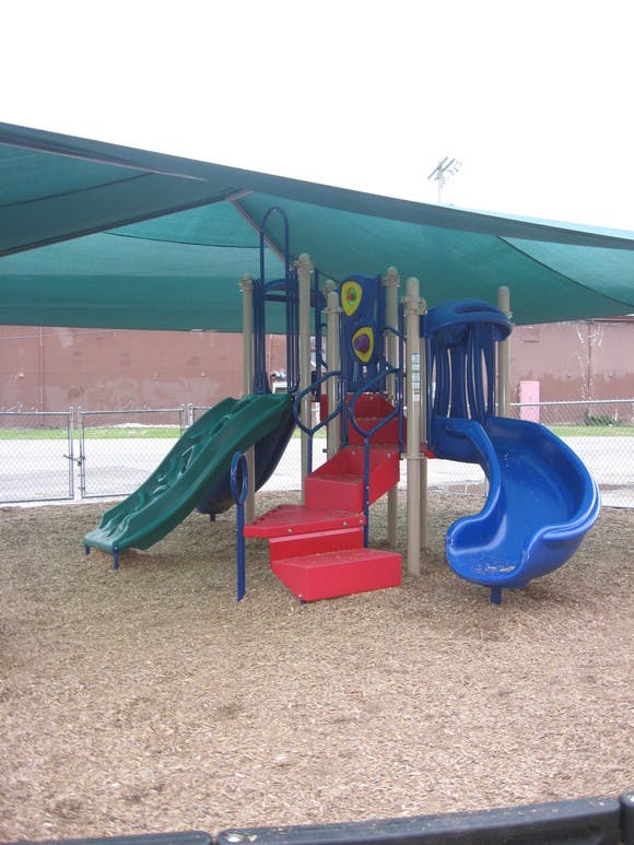Playground structure with multiple slides and stairs under a shade canopy