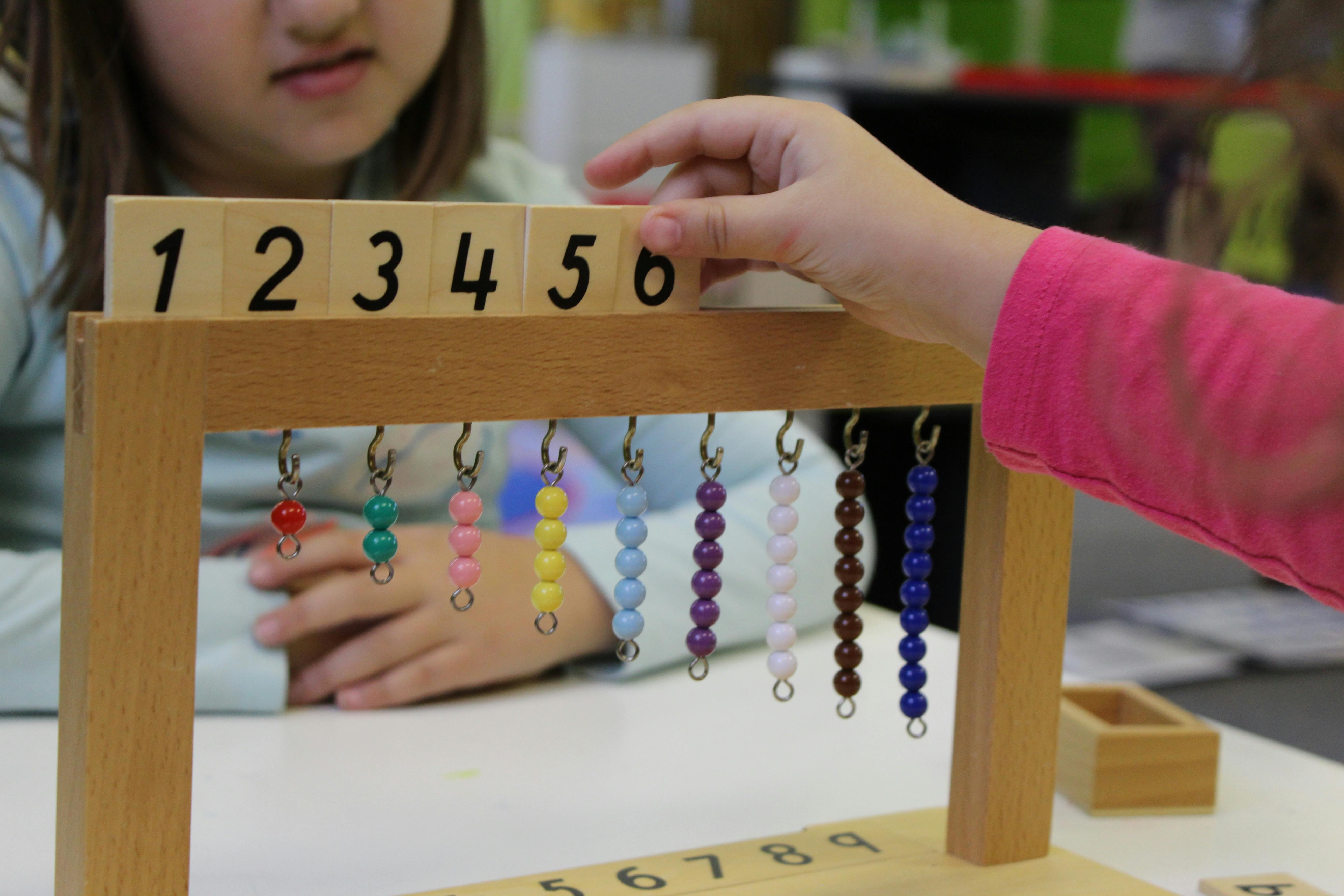 Child's hand touching a wooden number block with beads hanging below