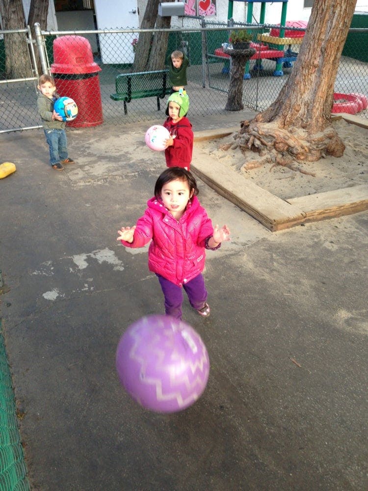 Child in pink jacket playing with a purple ball on a playground