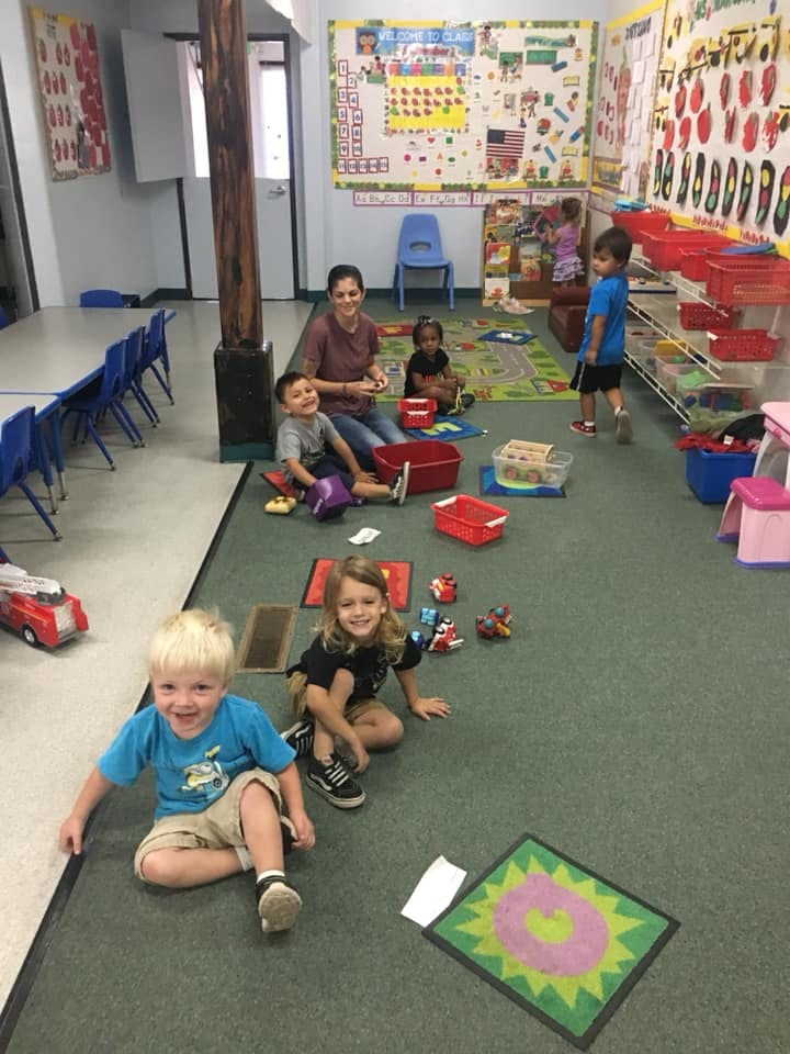 Adult and children playing with toys on the floor in a classroom