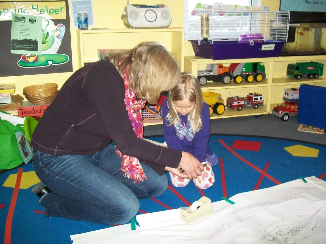 Adult and child kneeling on floor, looking at an object