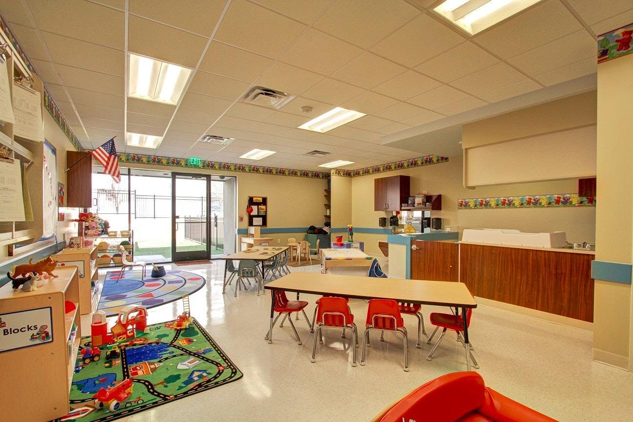 Empty classroom with small tables and chairs, play mats, and storage units