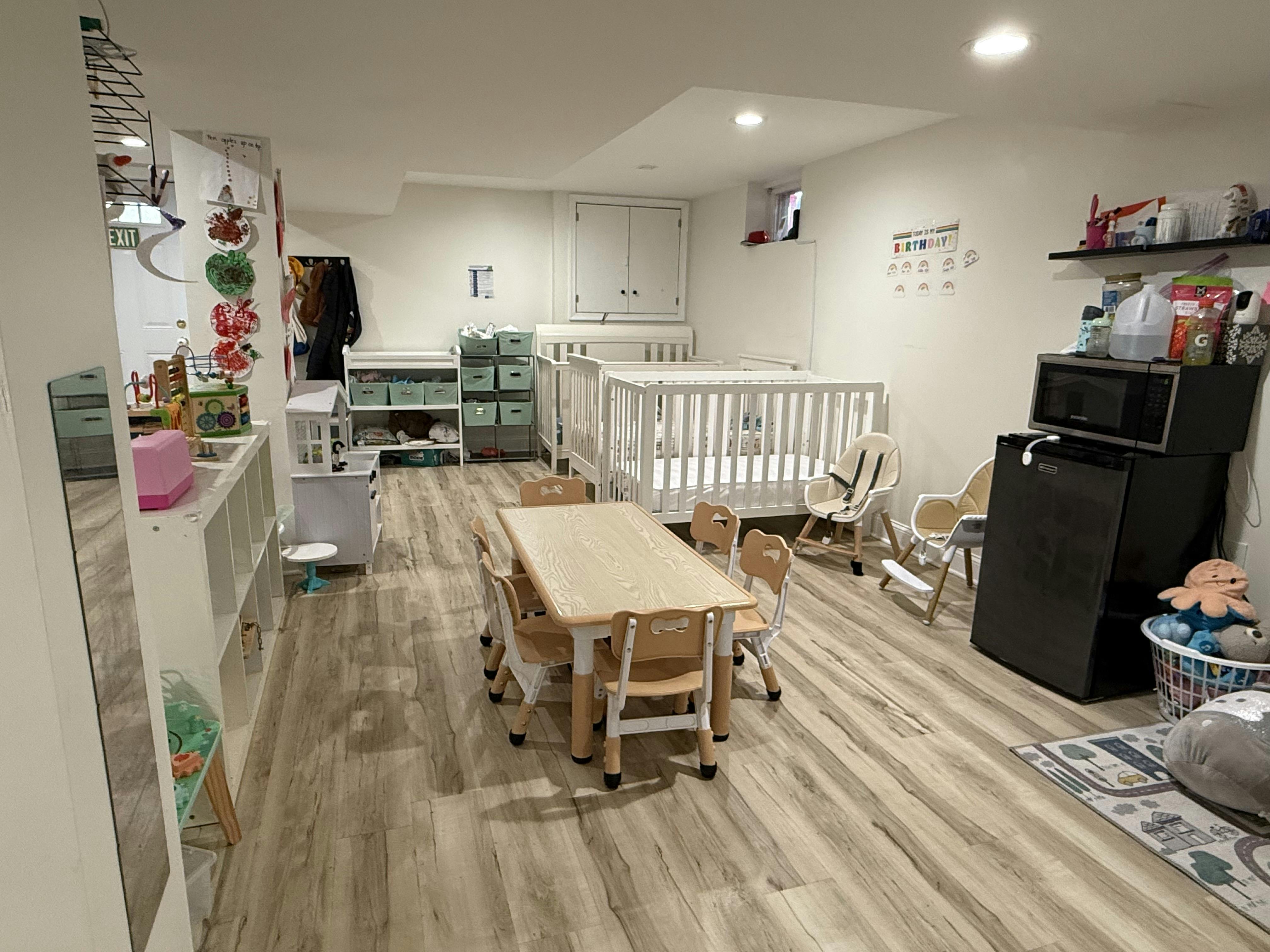 Childcare room with a central table, small chairs, and multiple cribs