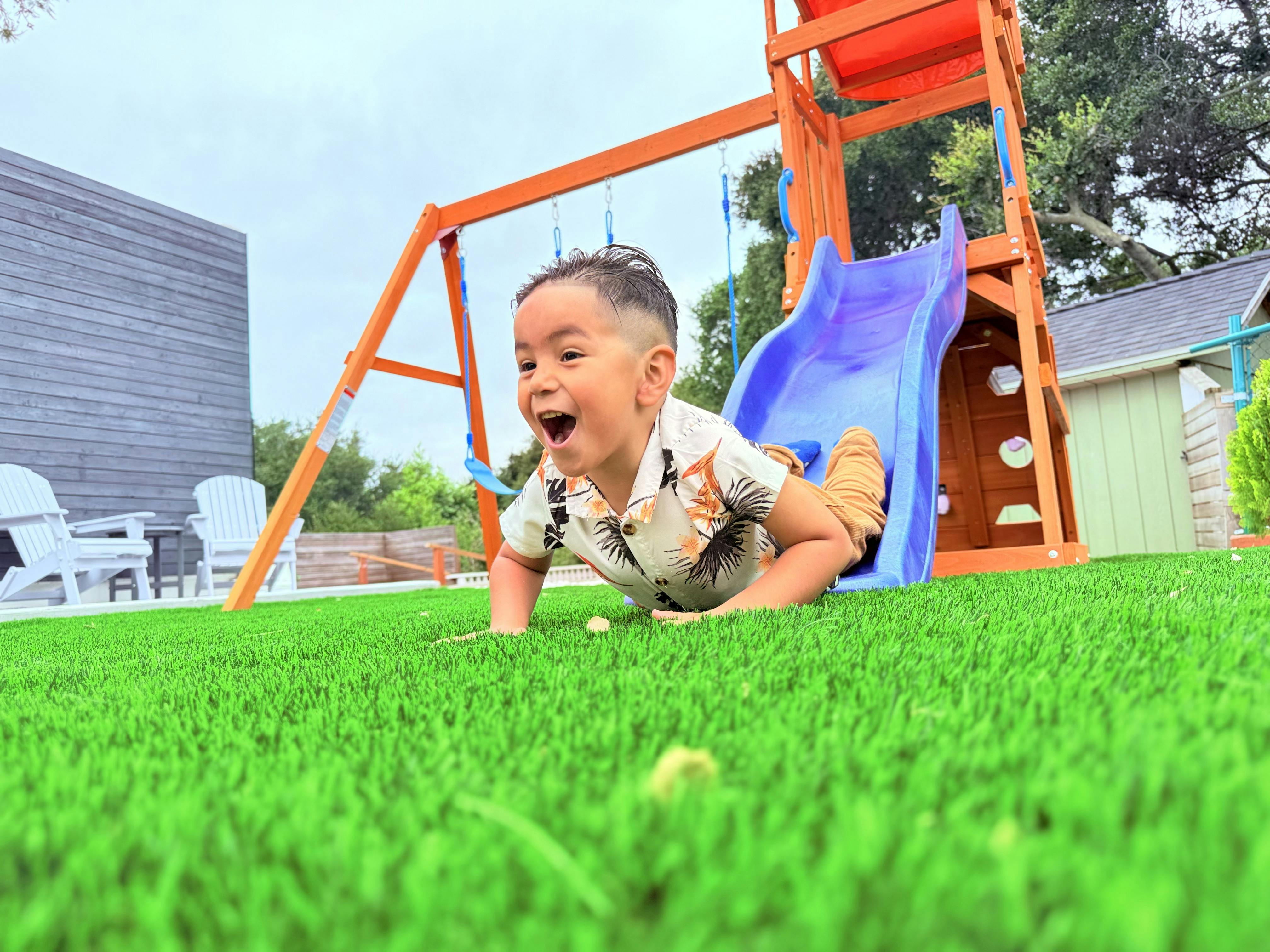 Child crawling on grass next to a playground slide