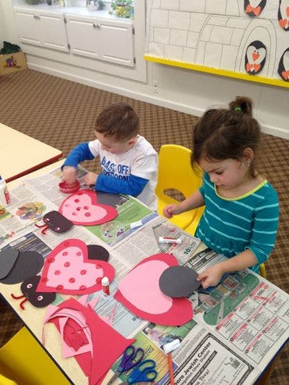 Two children doing crafts at a table with heart-shaped cutouts