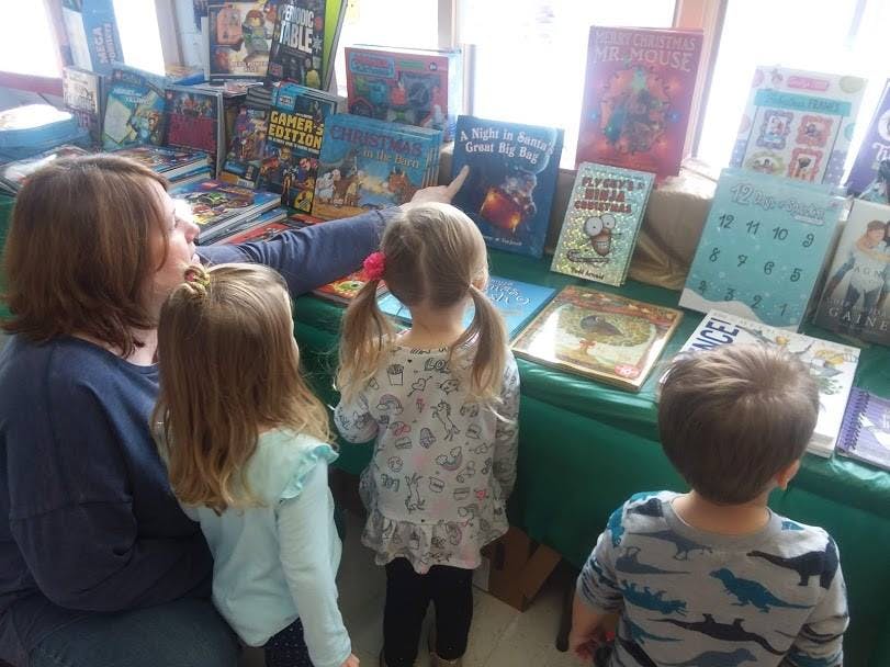 Person and two children looking at books on a table