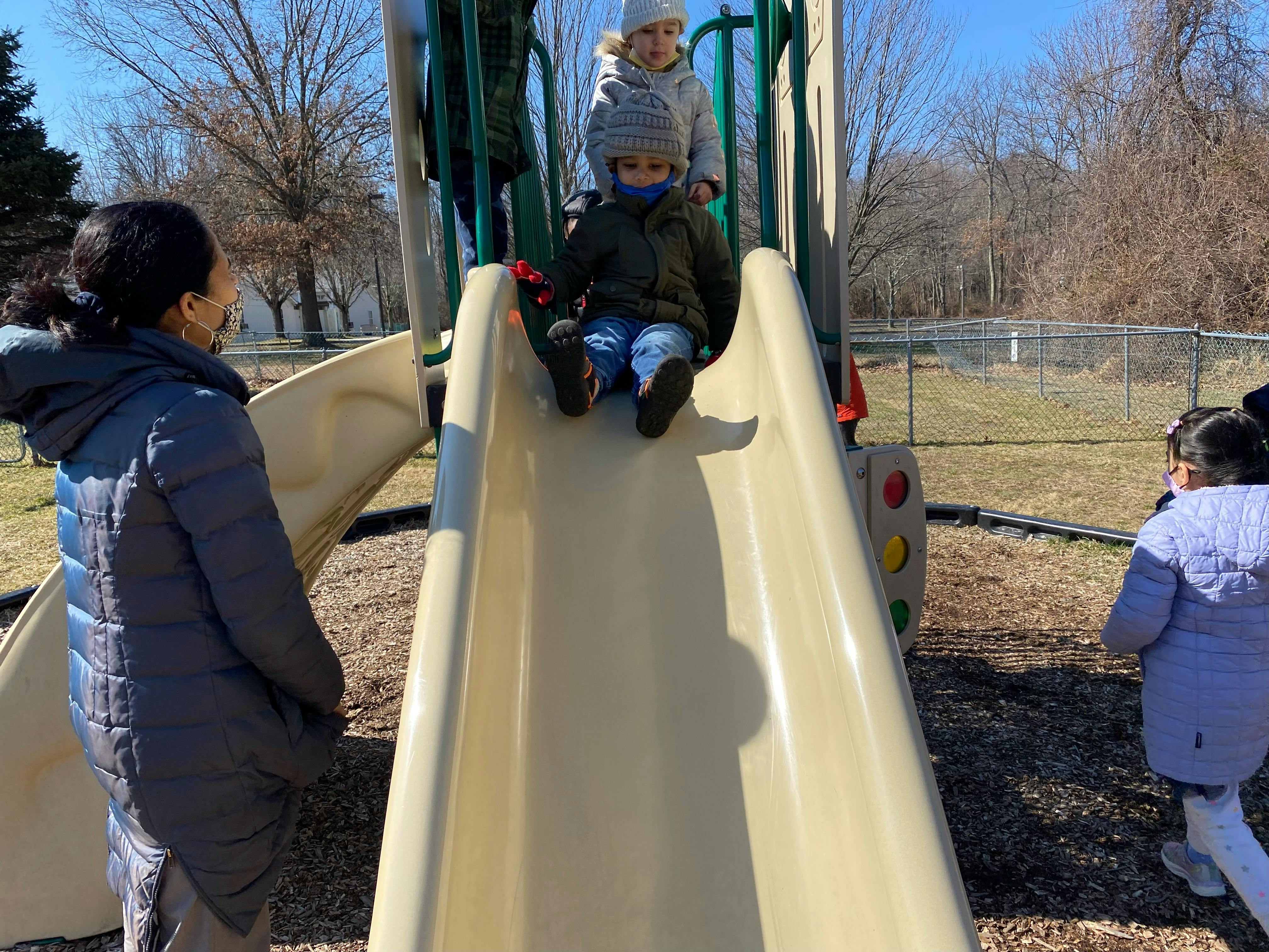 Child on a playground slide with an adult nearby