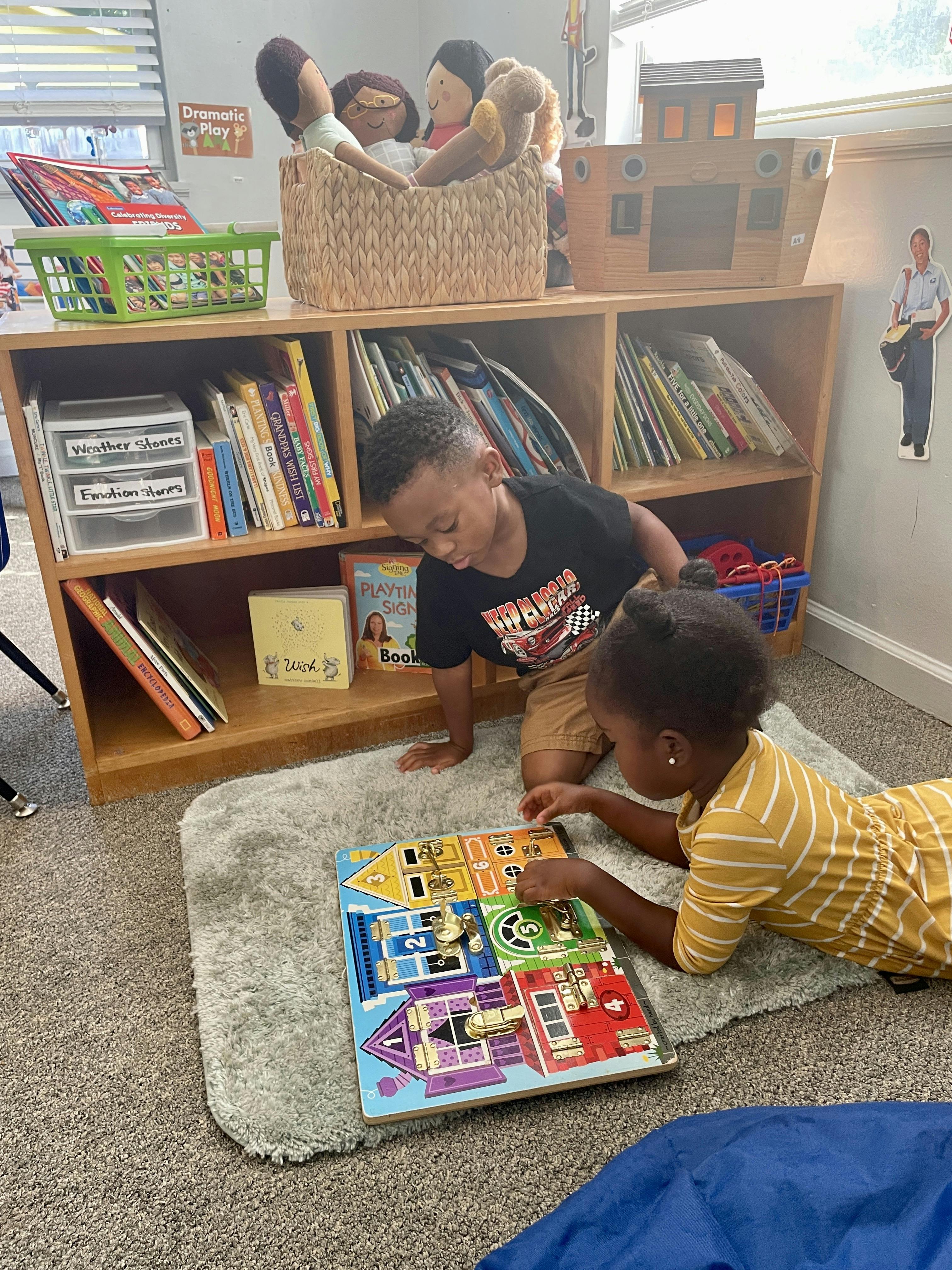 Two children playing with a latch puzzle board on a rug in a classroom