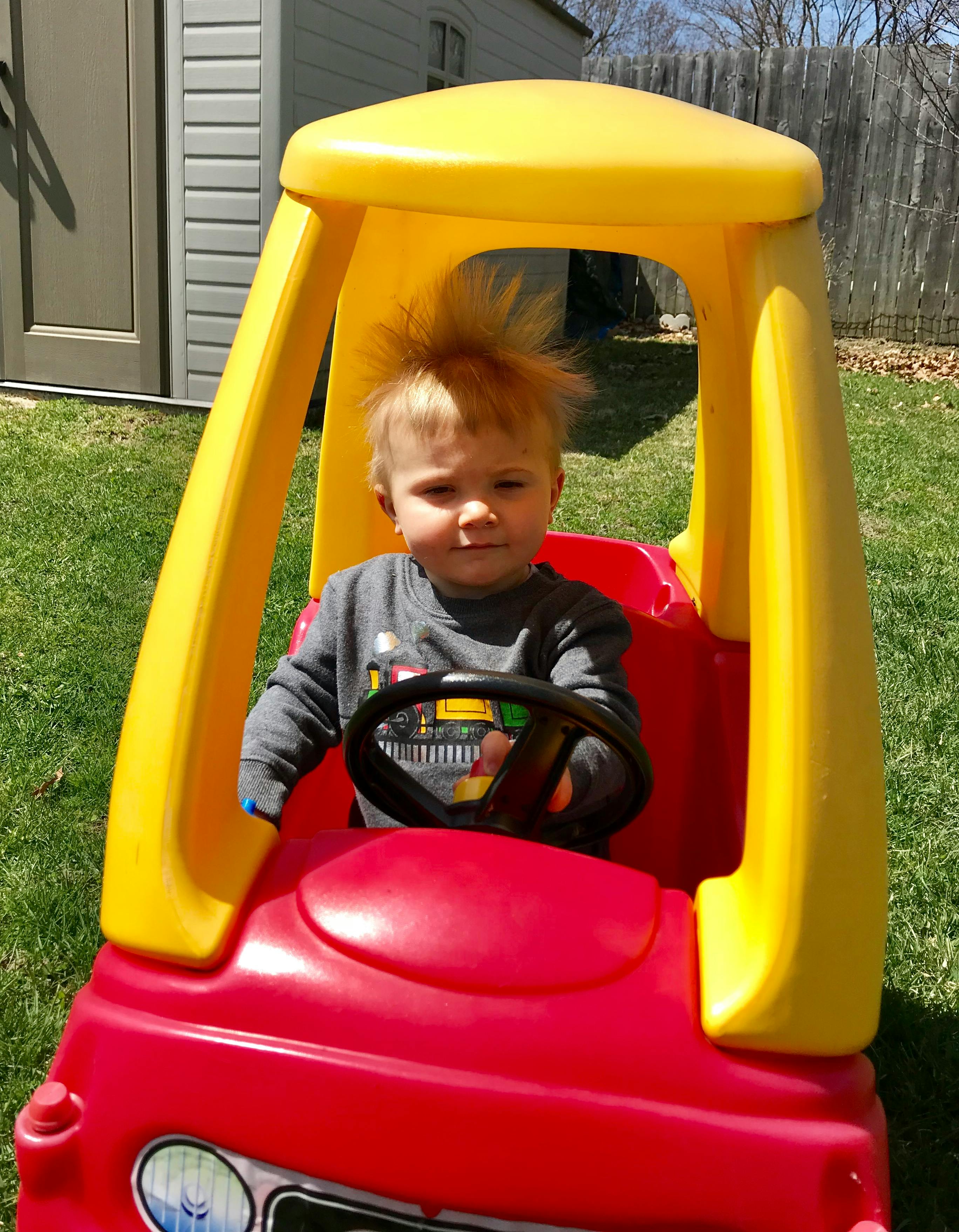 Child sitting in a plastic toy car on a lawn