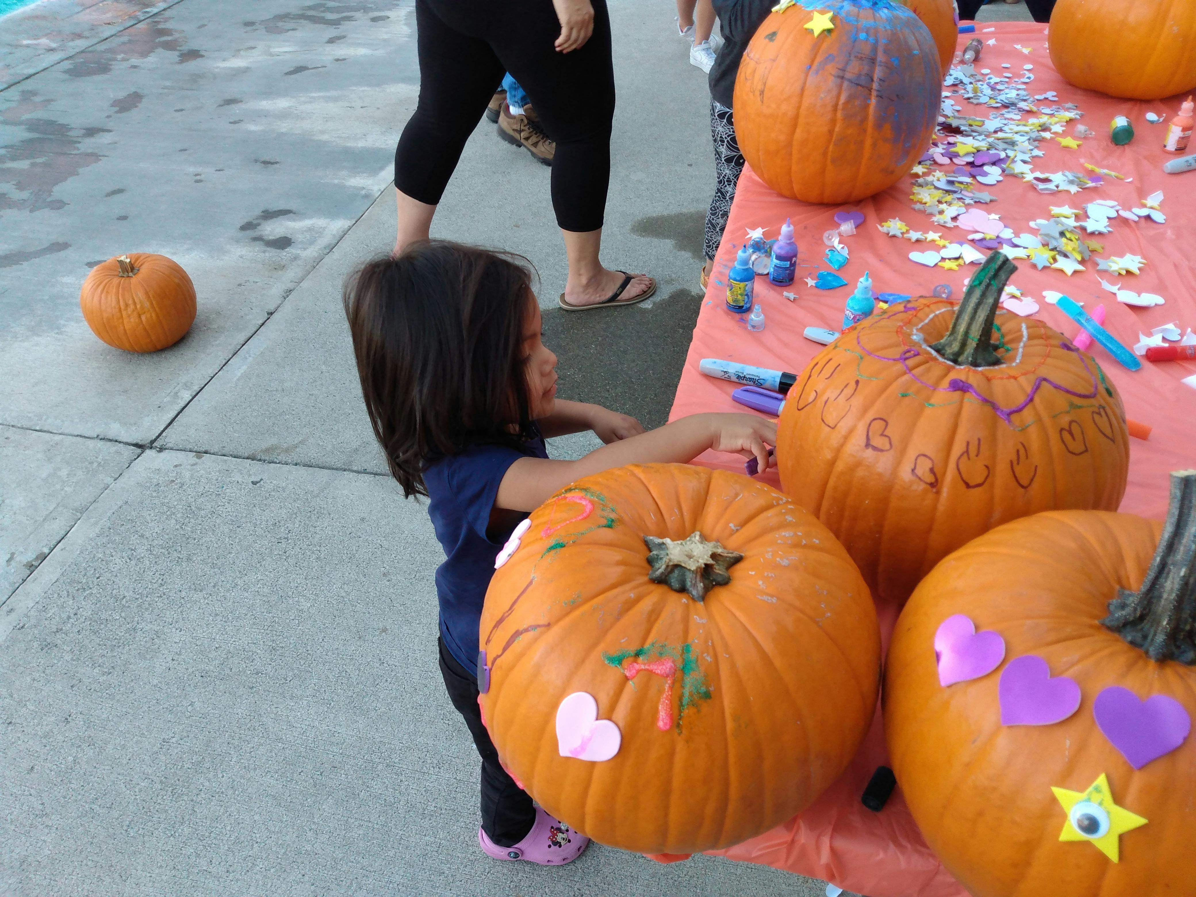 Child decorating a pumpkin on a table with other decorated pumpkins